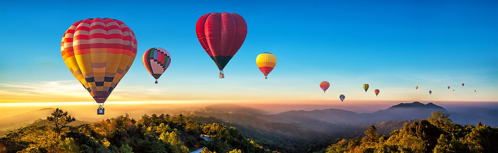 Hot air balloons in the air over a scenic valley