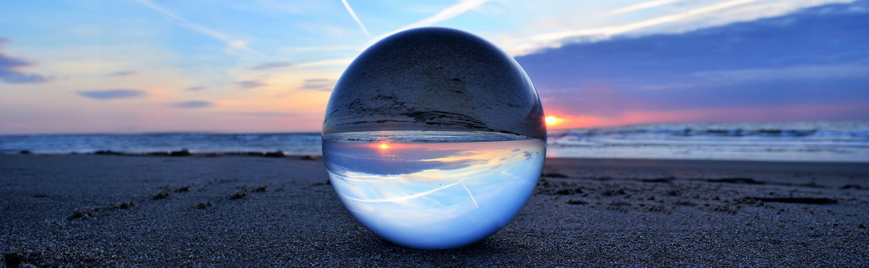 A mirrored sphere on a beach with waves in the background